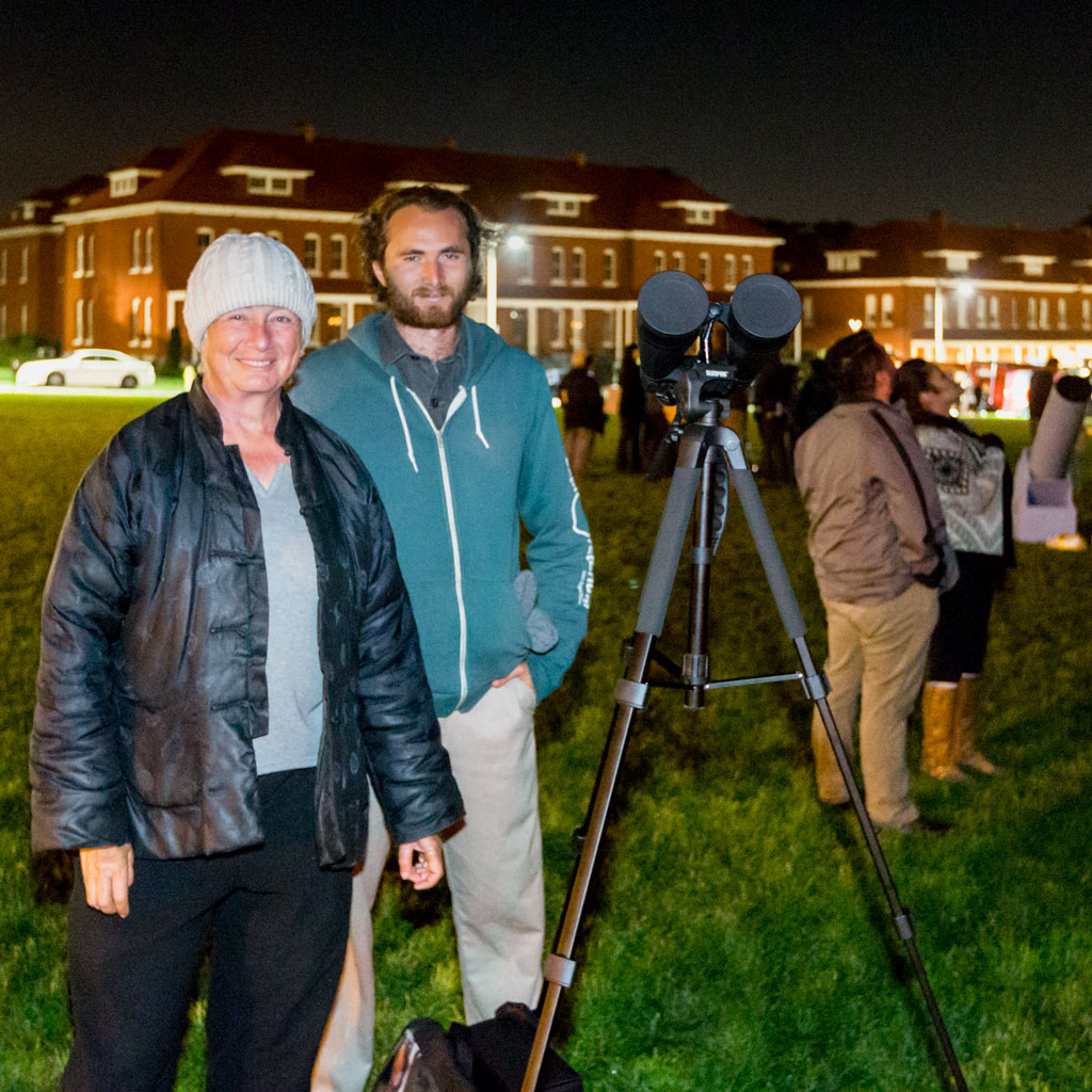 Woman and man next to telescope at night