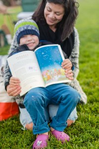 Child holding book open while in woman's lap