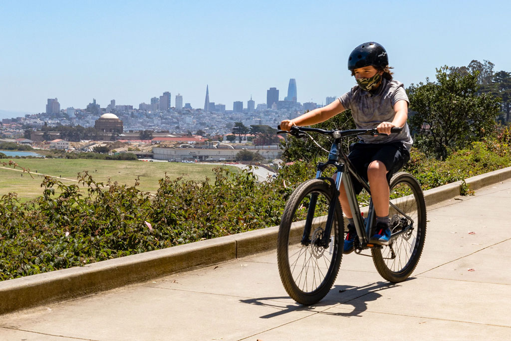 Boy with mask and helmet on riding bike down Crissy Field