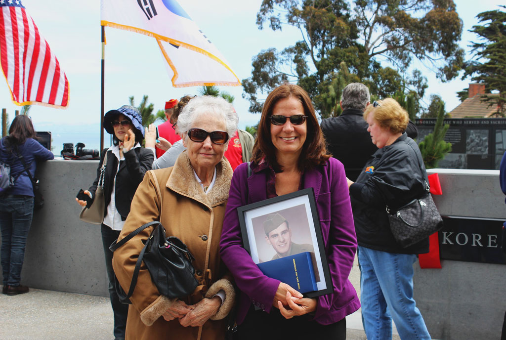 A couple women holding medal and photo at Korean War Memorial