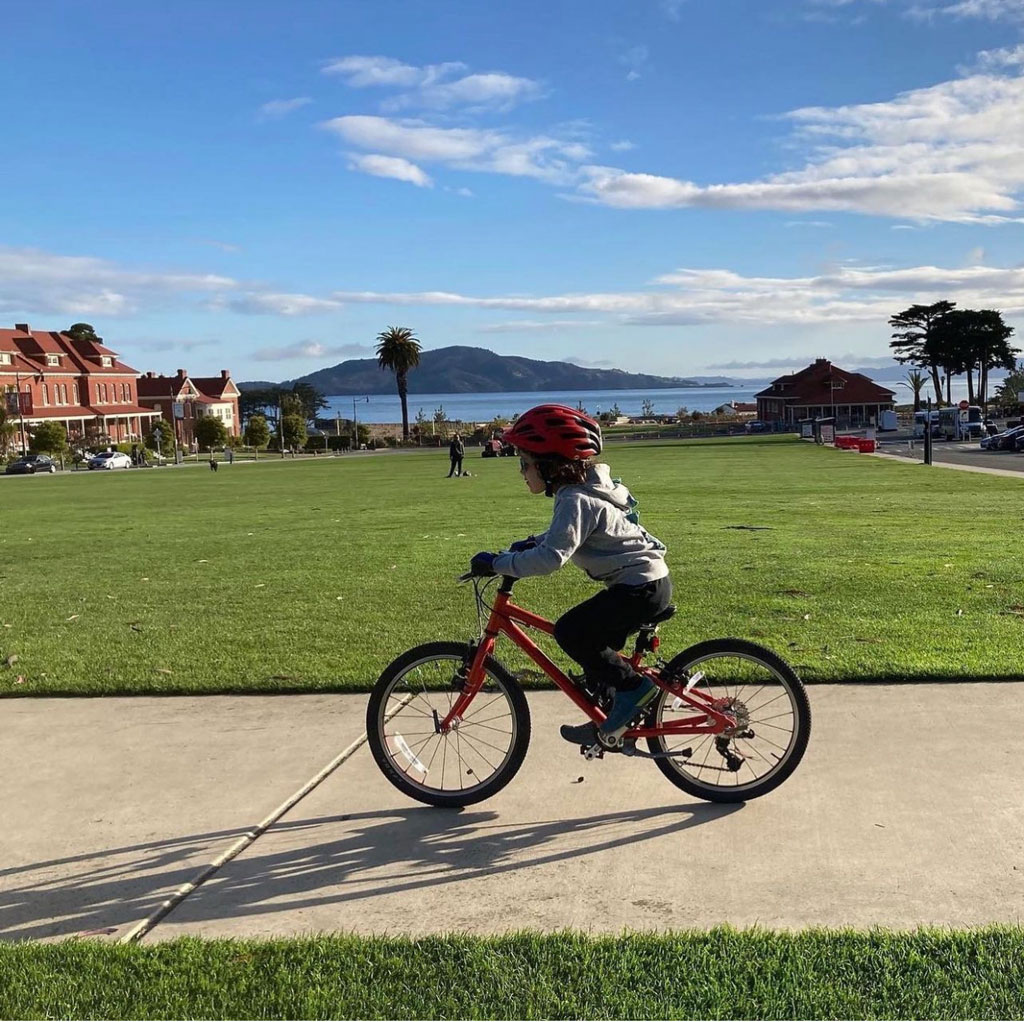 Child in helmet biking on sidewalk at Main Parade Lawn