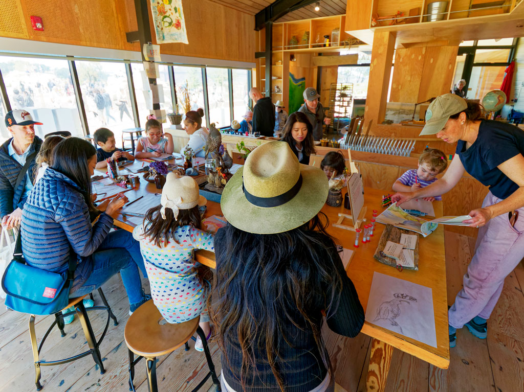 Adults and children drawing around table inside Field Station