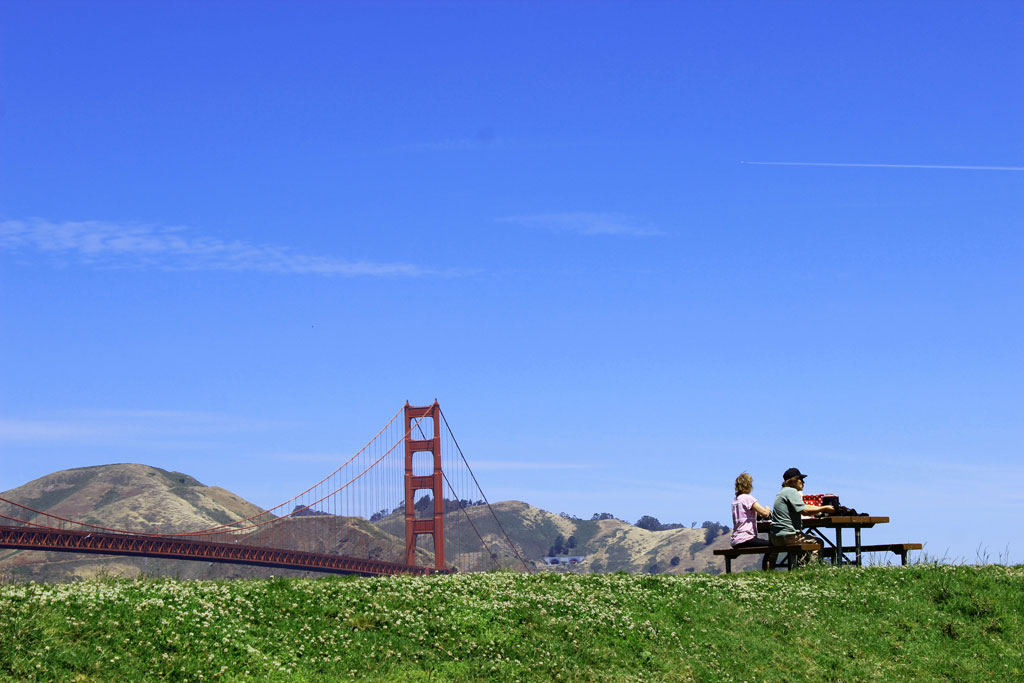 A couple visitors sitting at picnic table on hill with Golden Gate Bridge in background