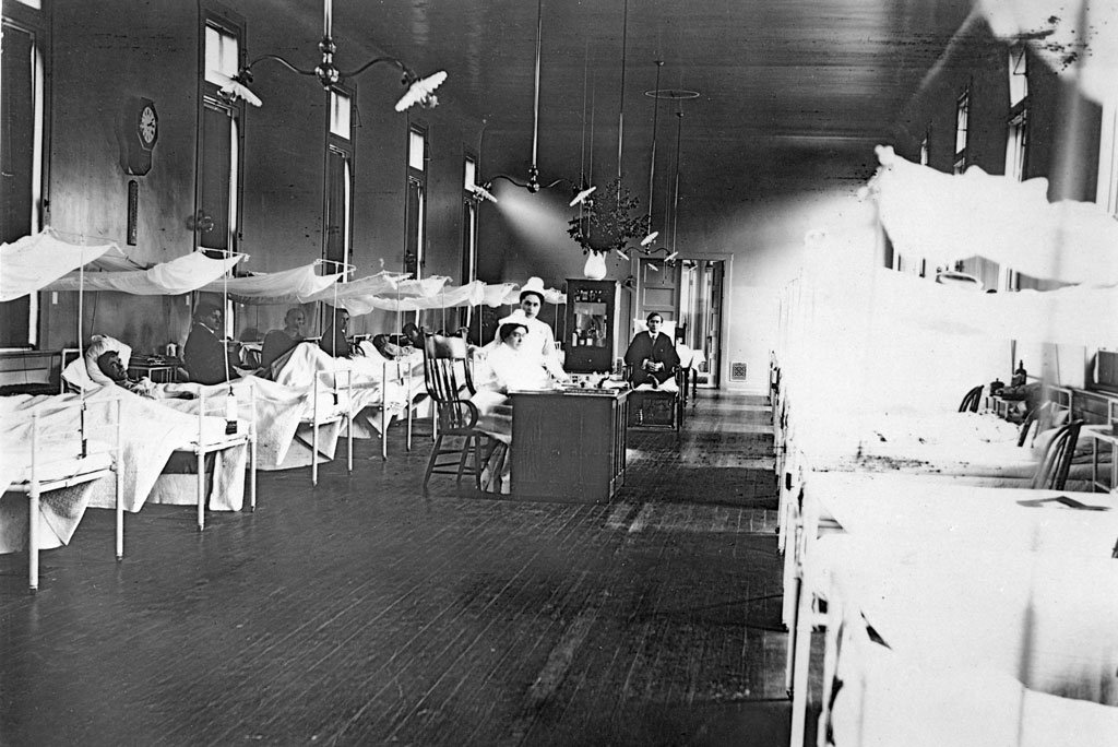 Nurses, doctor, and patients in Surgical Ward. Beds lined up on both sides.