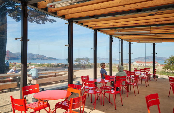 Red tables and chairs inside the Pavilion, with two visitors seated.