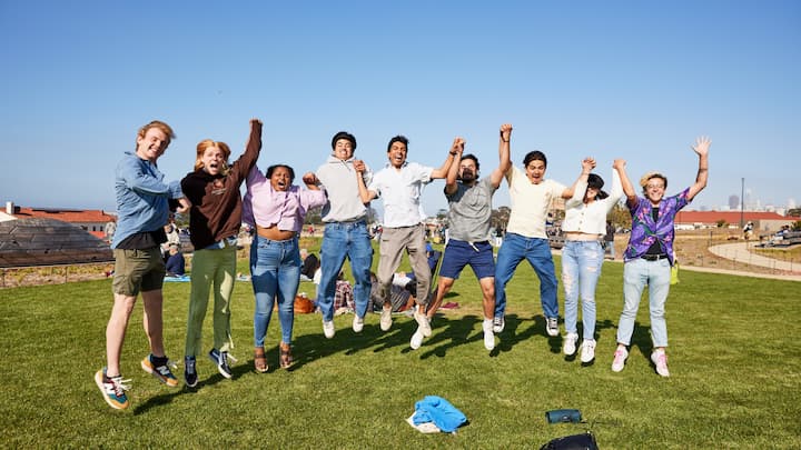 Seven people jumping on a lawn at Presidio Tunnel Tops.