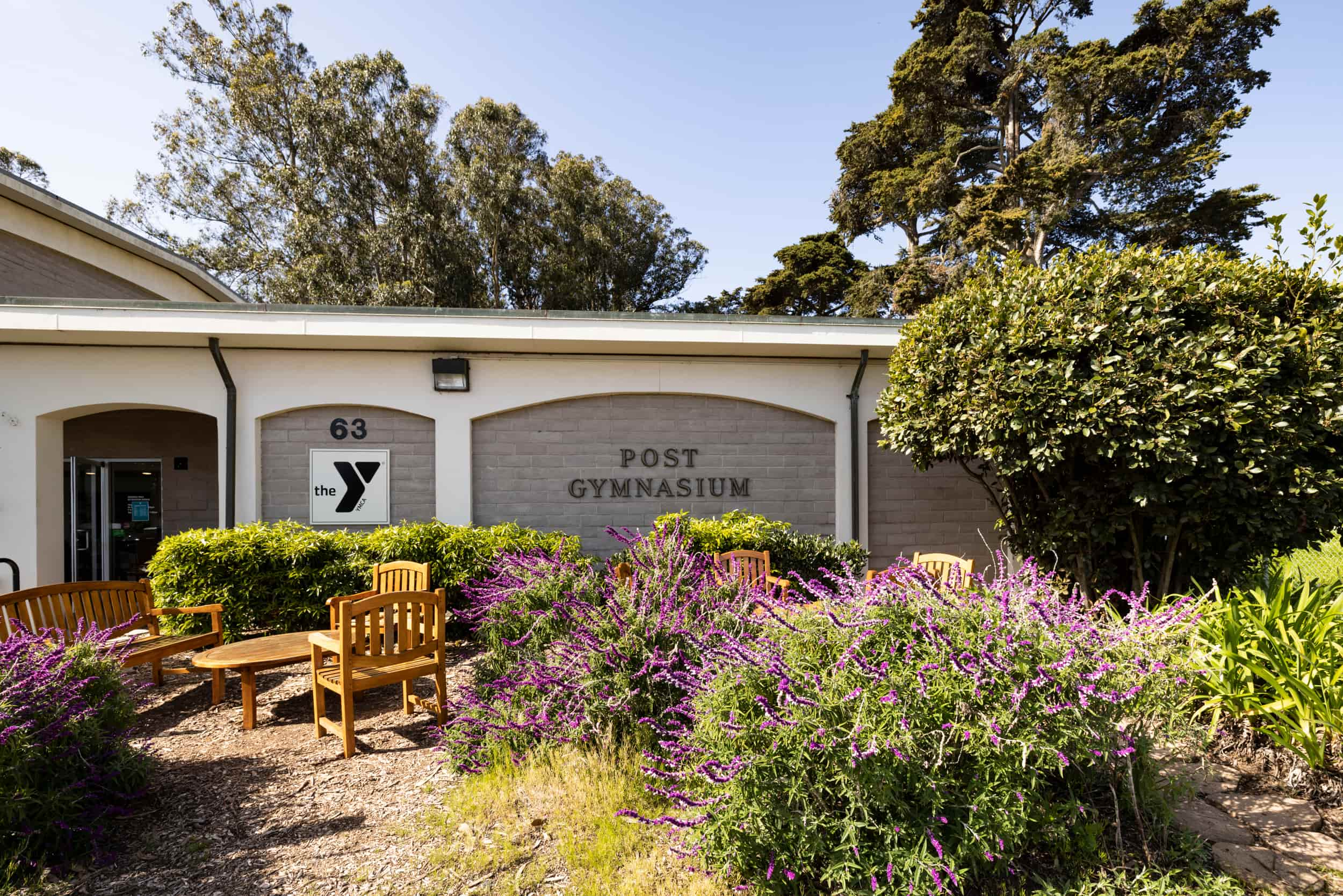 External photo of Presidio Community YMCA. Features the side of the building with plants in front of the sign that says Post Gymnasium