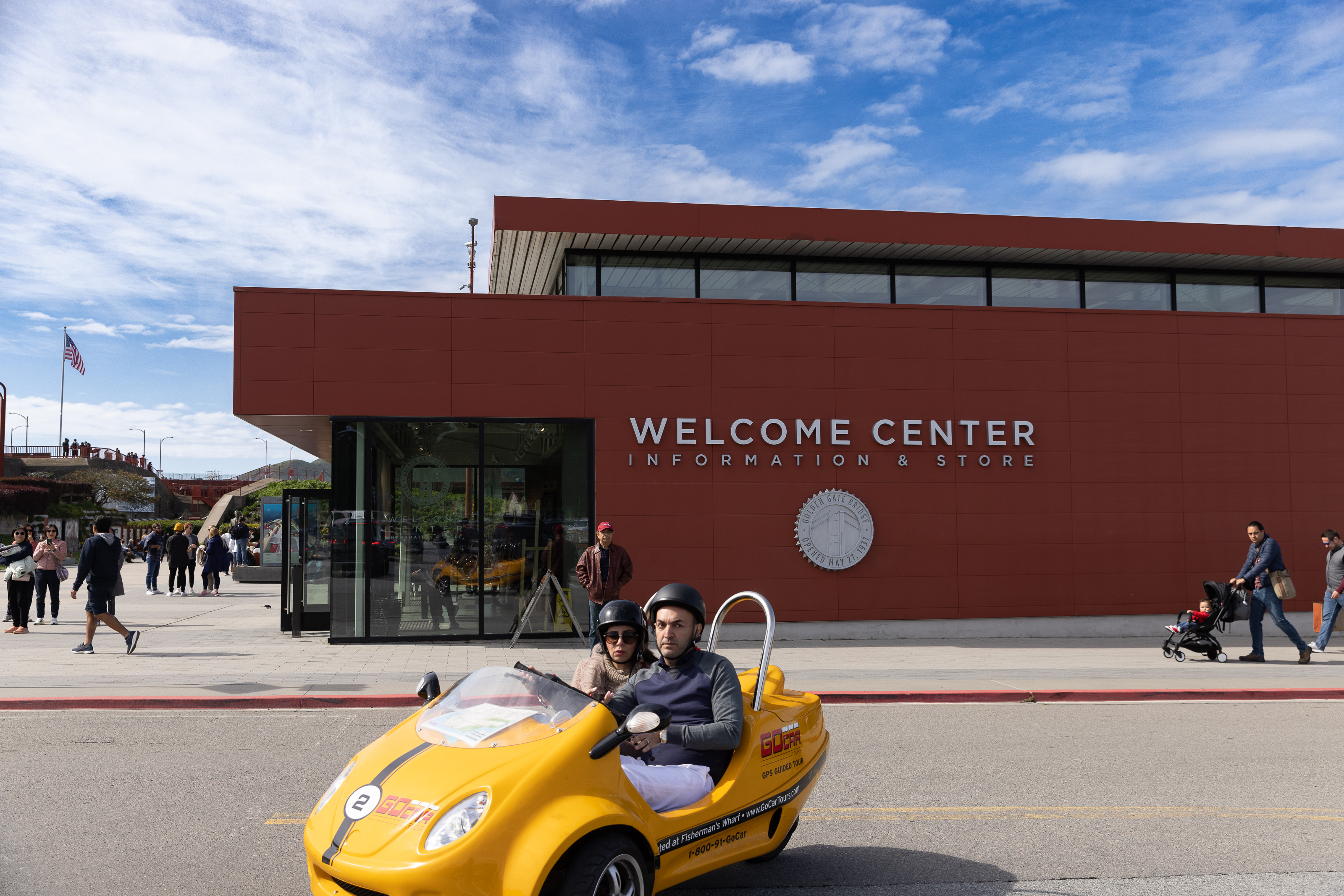 Little yellow tour cart with two people riding in it in front of the Golden Gate Bridge Welcome Center