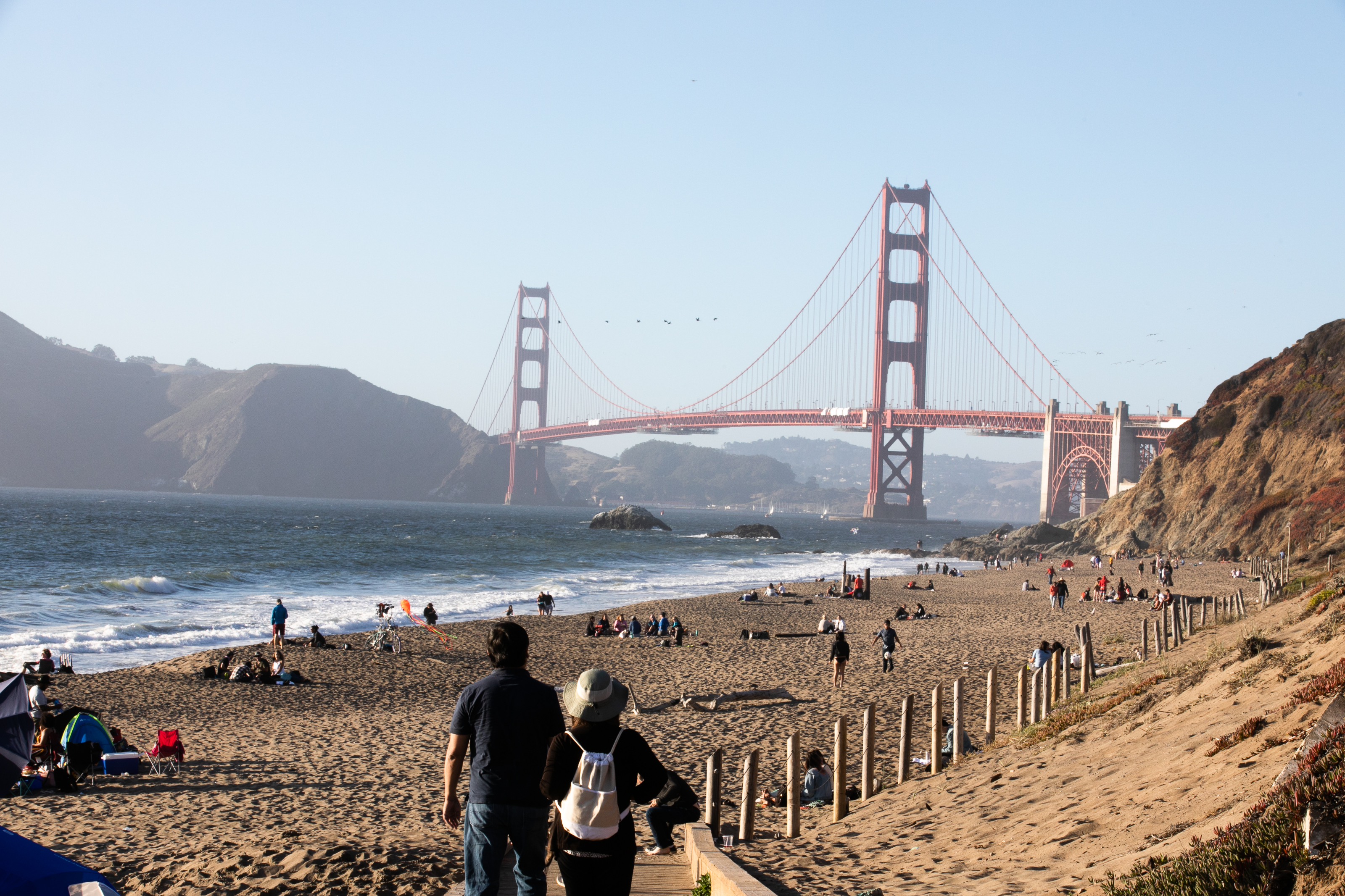 Man and woman looking out over Baker Beach at the Golden Gate Bridge.